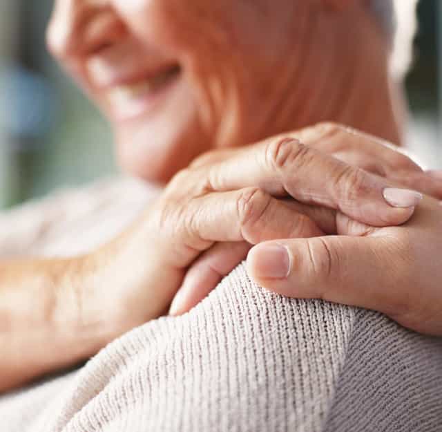 Closeup of a caring hand on the shoulder of an elderly woman.