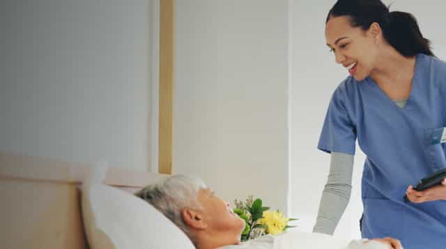 A female nurse helpfully addresses an elderly patient.